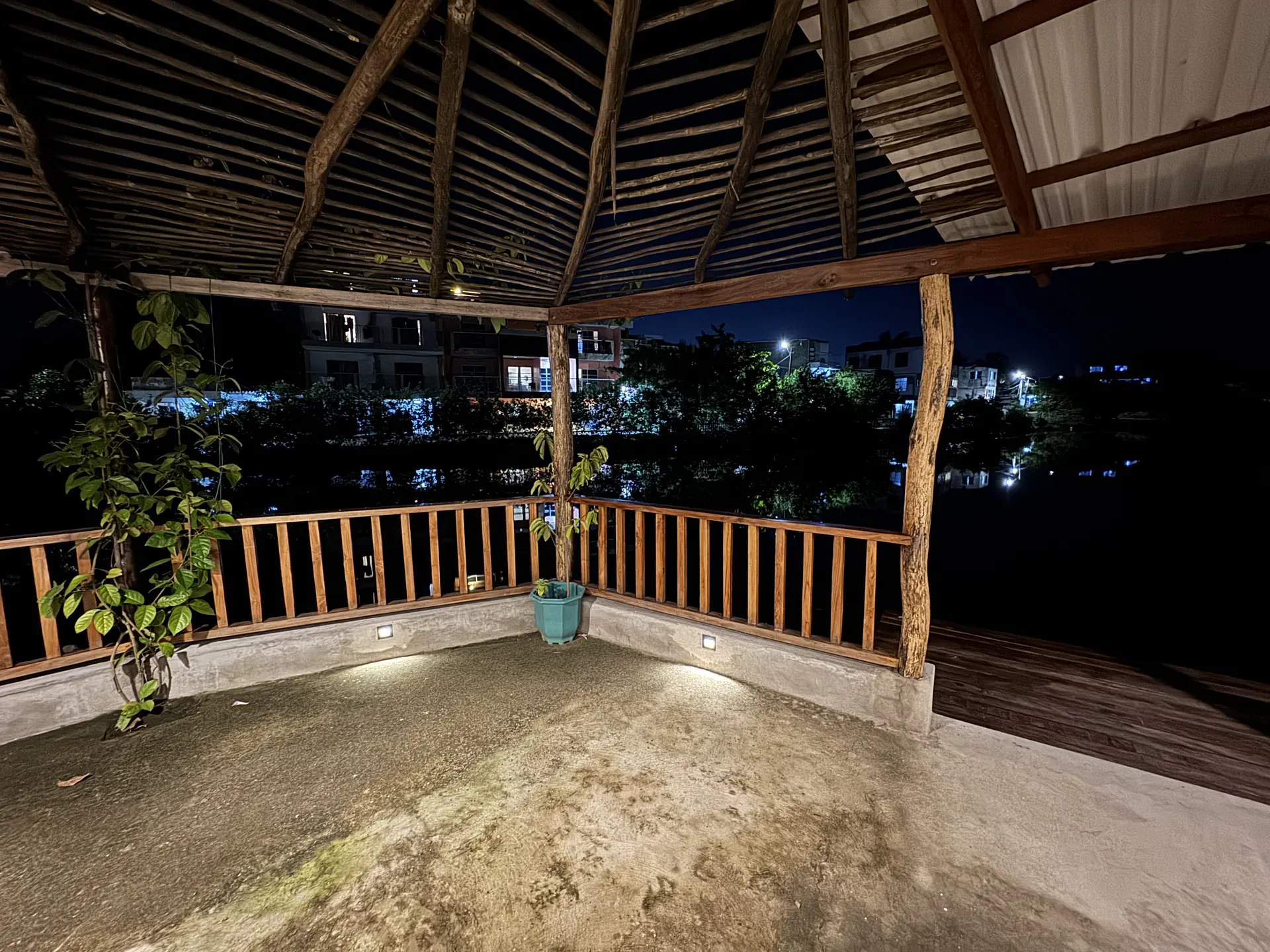Terraza nocturna con techo de palapa y vista al lago, barandal de madera y piso de concreto